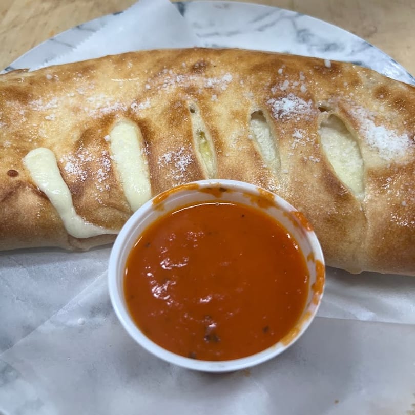Golden-brown calzone with melted cheese visible through slits, served with a side of red marinara sauce.